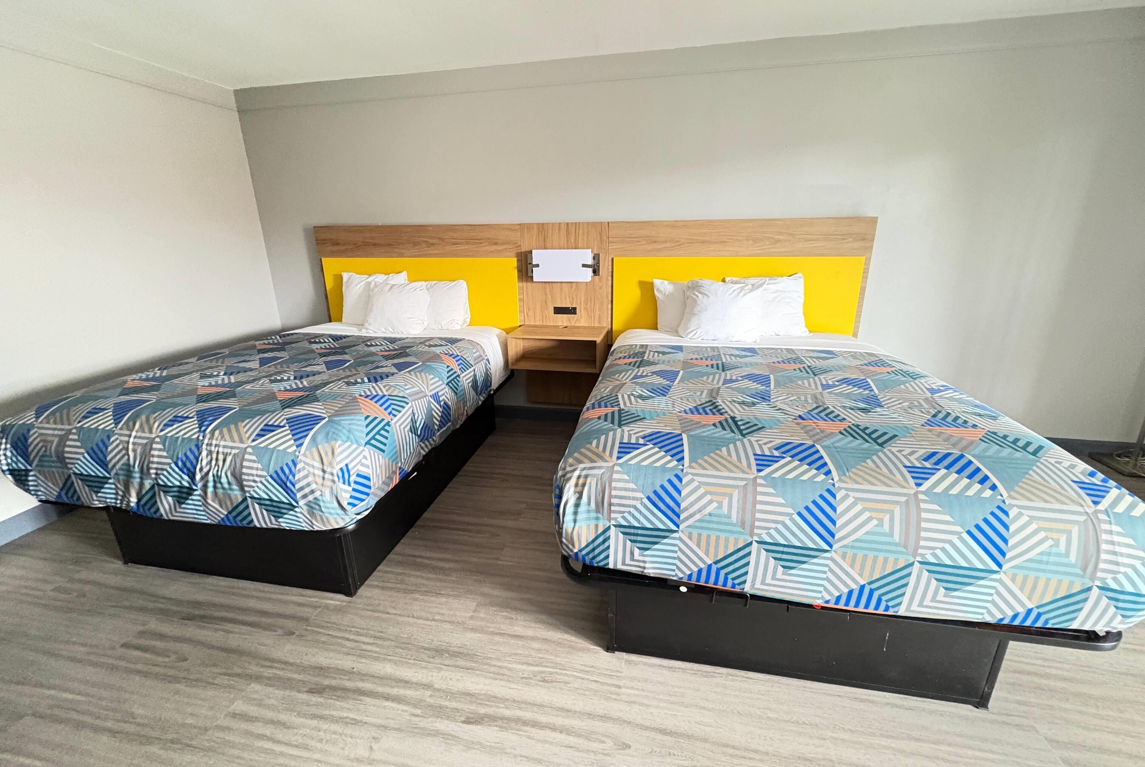 Habitación de hotel con dos camas, cabecero de madera y una mesita de noche con lámpara.
