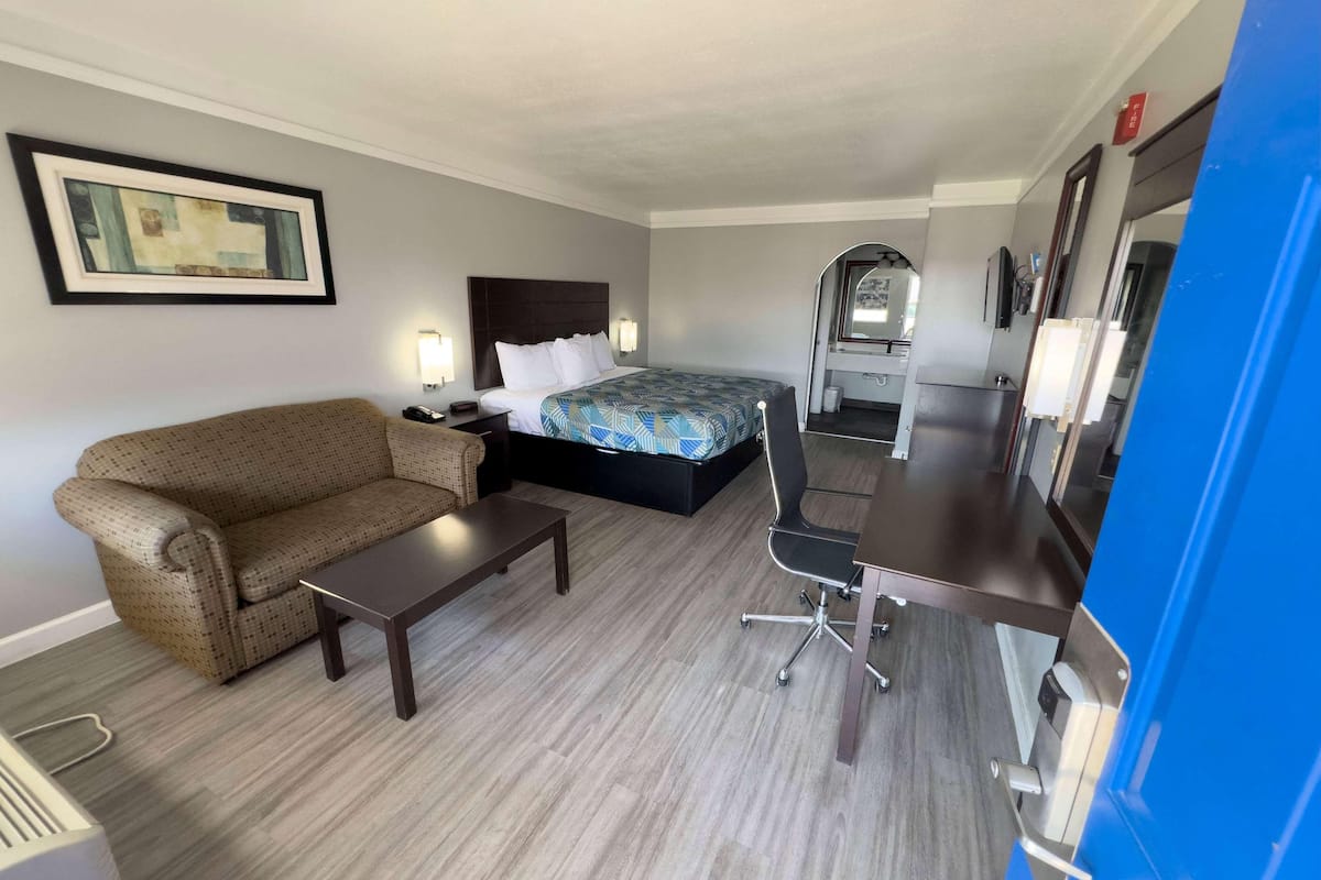 A hotel room with a bed, a sofa, a desk, and a kitchenette.