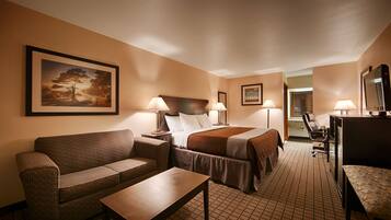 A hotel room with a bed, two bedside lamps, a sofa, a small table, and a desk with a chair.