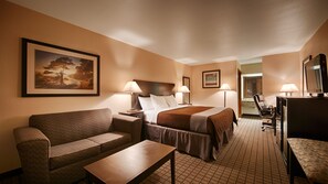 A hotel room with a bed, two bedside lamps, a sofa, a small table, and a desk with a chair.