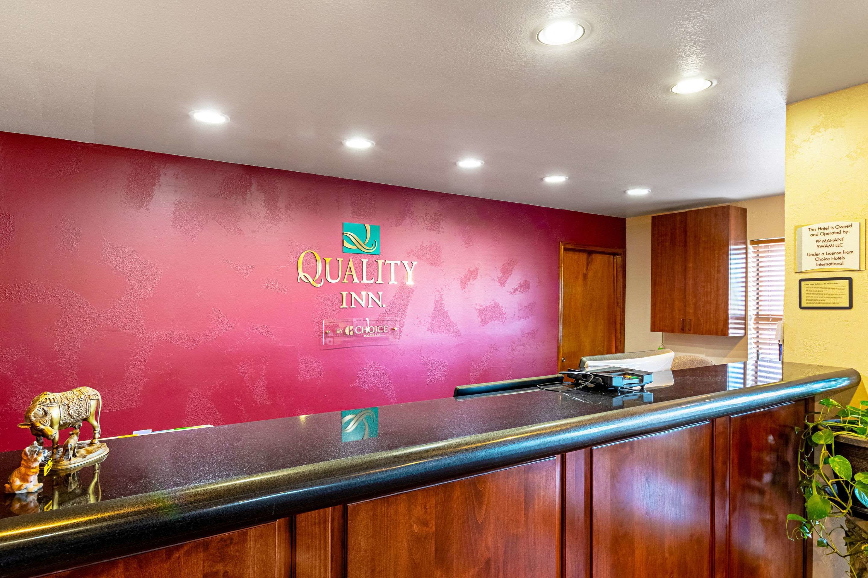 Et receptionsområde med rød væg, en receptionsdisk og et skilt, der står 'Quality Inn by Choice'.
