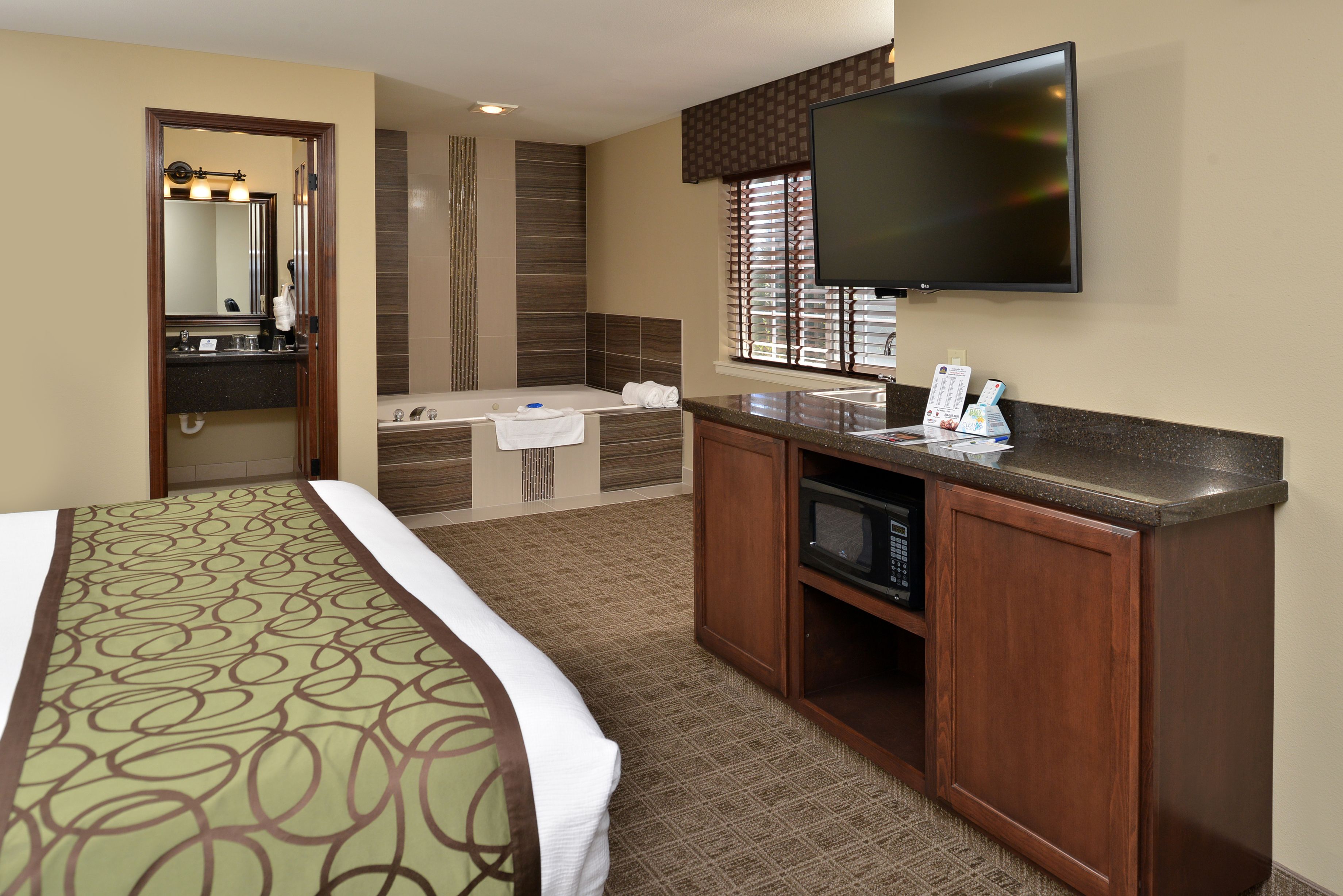 A hotel room with a large bed, a bathroom with a bathtub, a flat-screen TV, and a wooden cabinet.