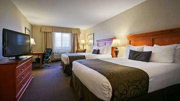A hotel room with two beds, a TV, a desk, and a chair.