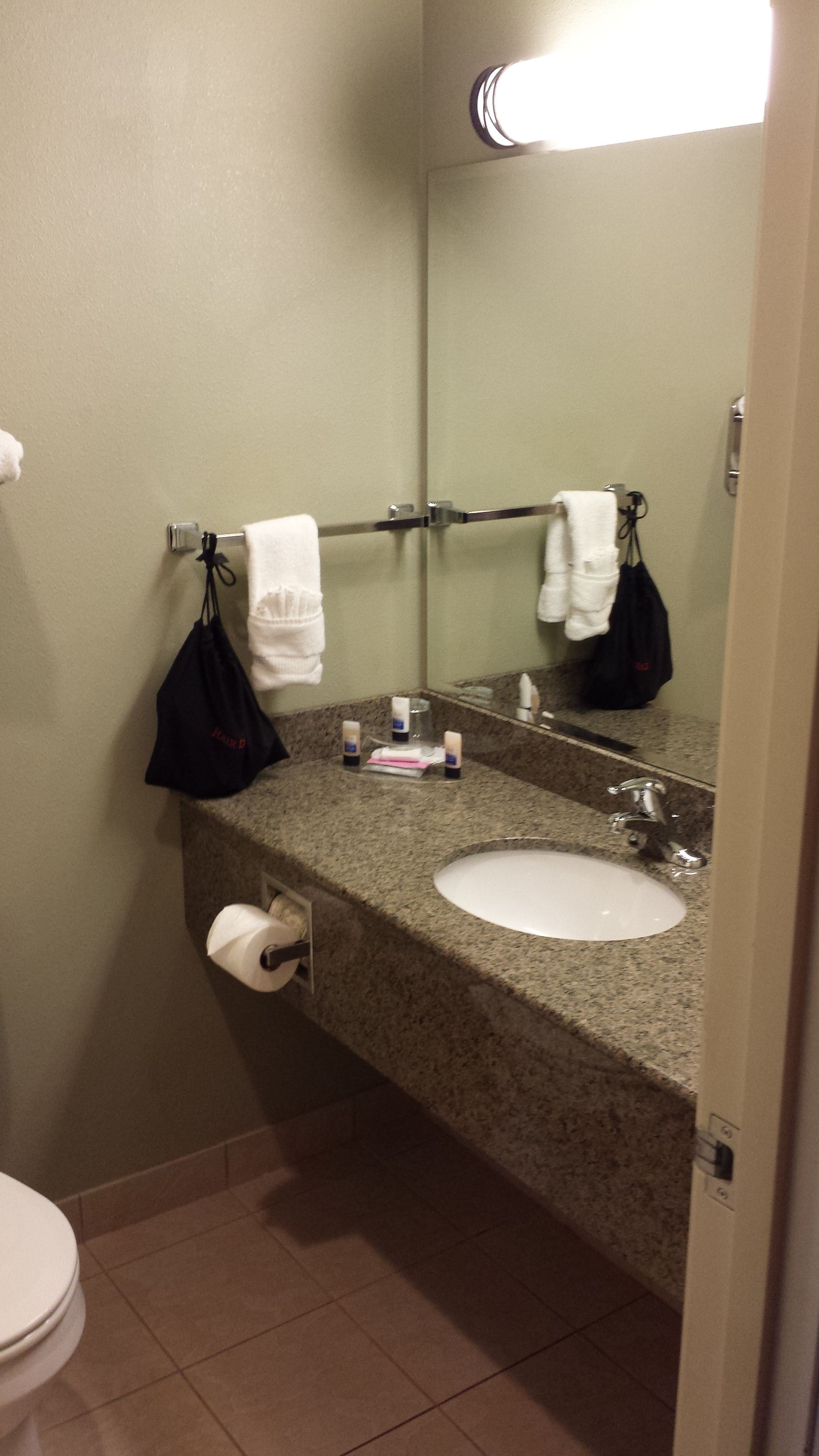 A bathroom with a granite countertop, a white sink, a mirror, and a towel rack.