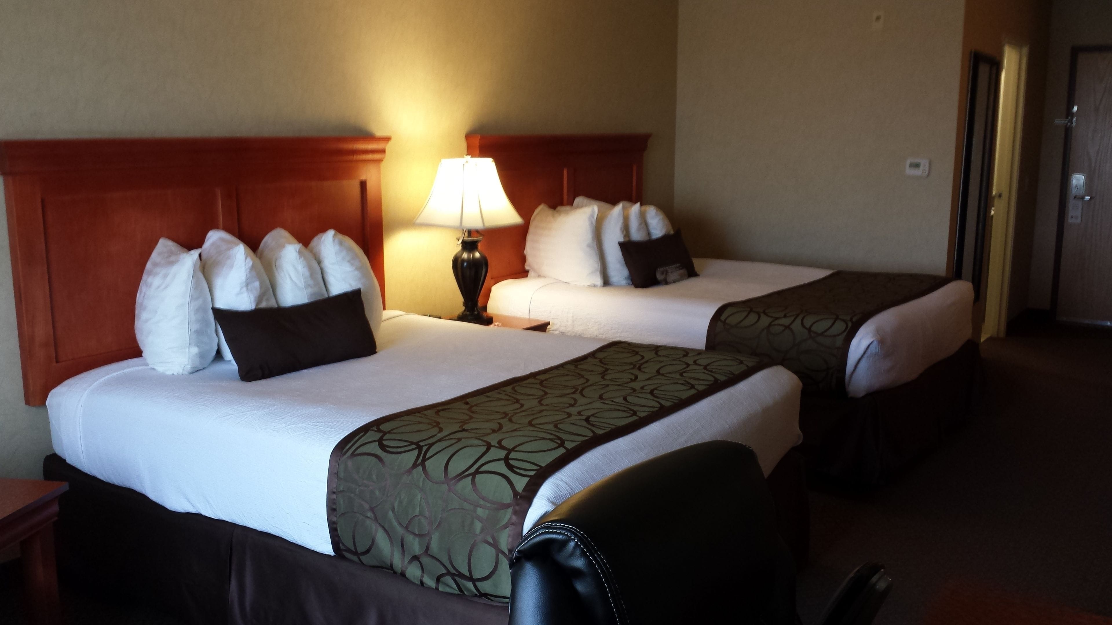 Two double beds with headboards, a bedside table with a lamp, and a door to the right.