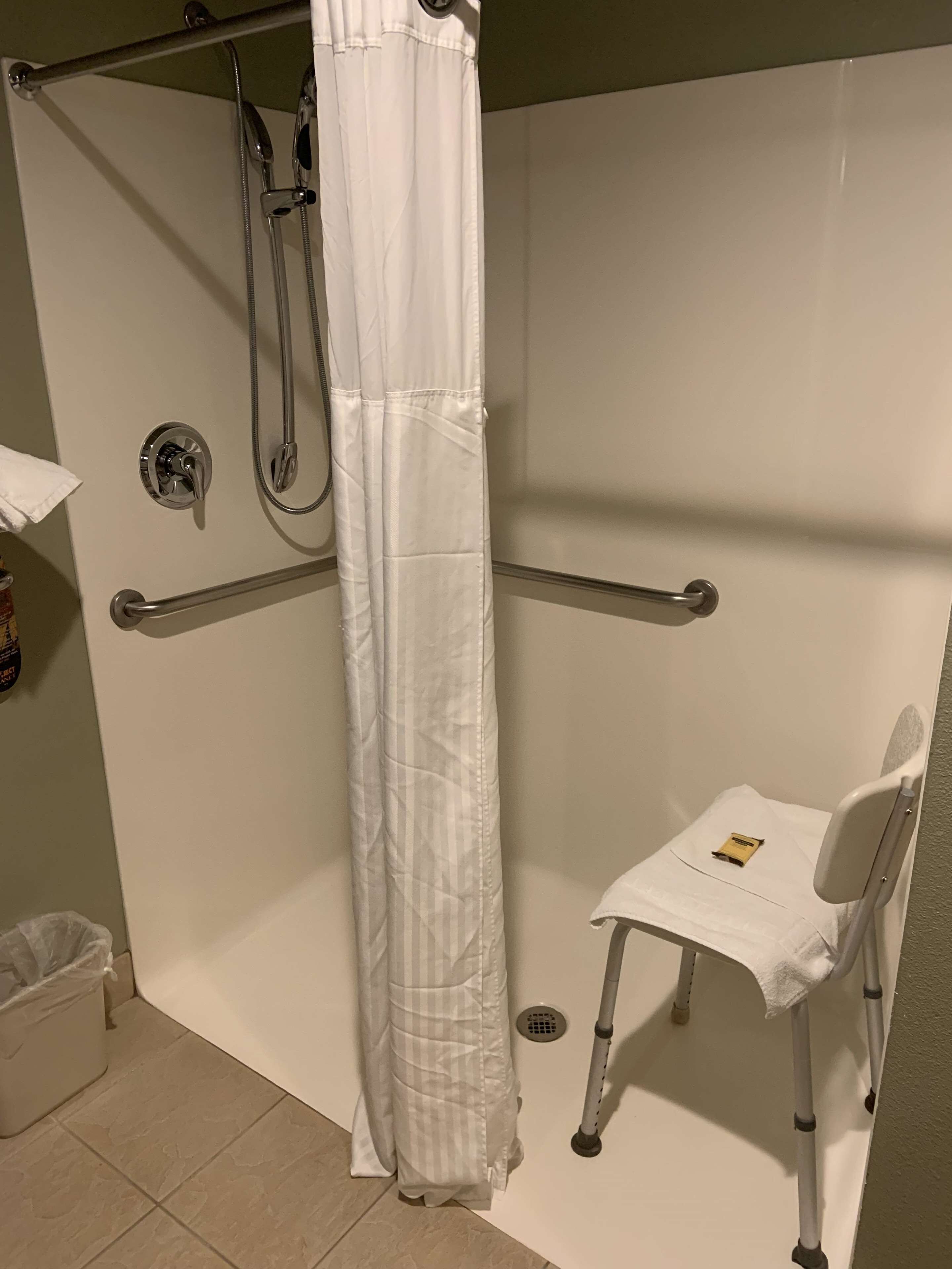 A shower area with a white shower curtain, grab bars, and a wheelchair-accessible bench.