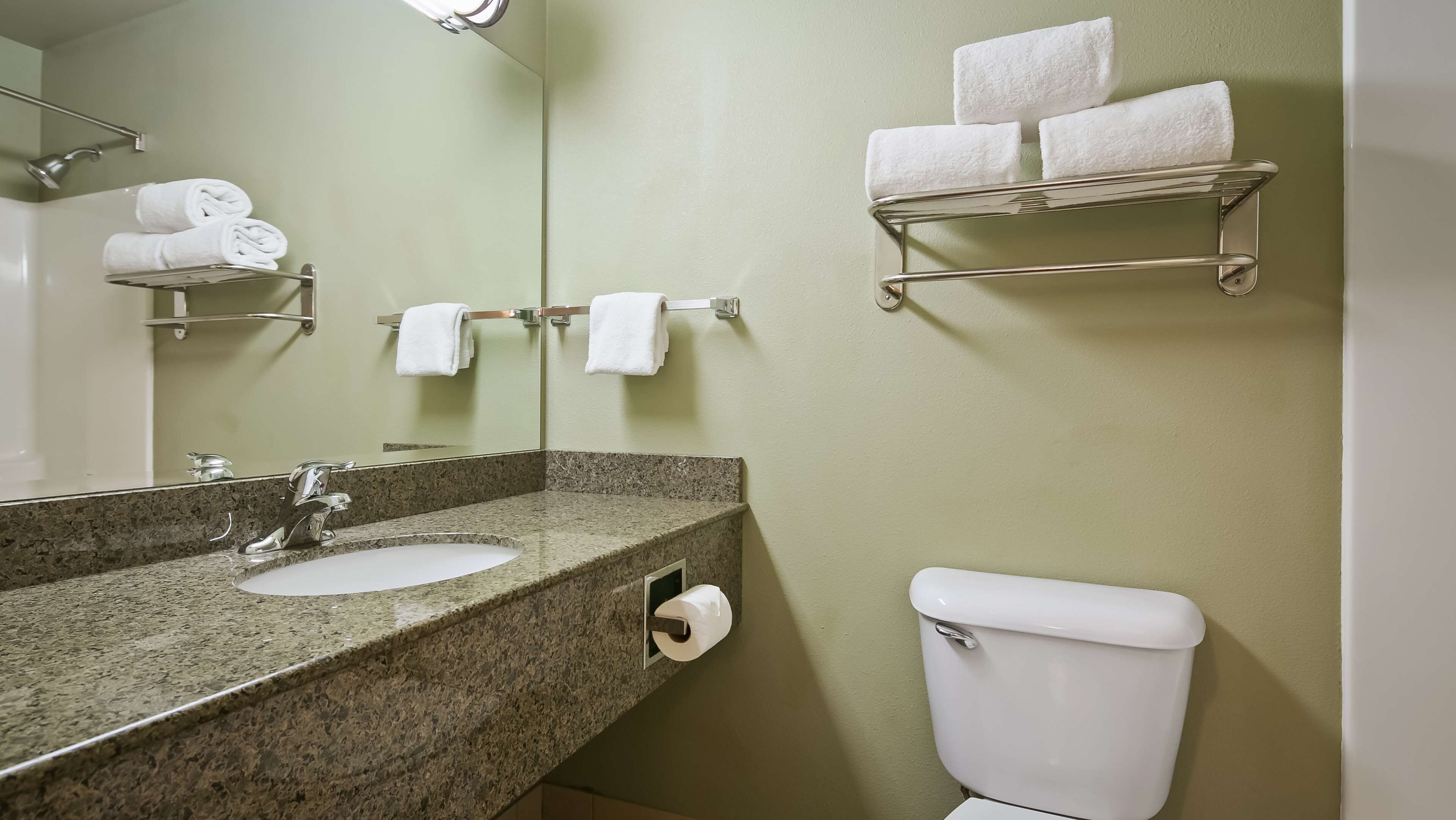 A bathroom with a granite countertop sink, a mirror, a toilet, and towel racks with folded towels.