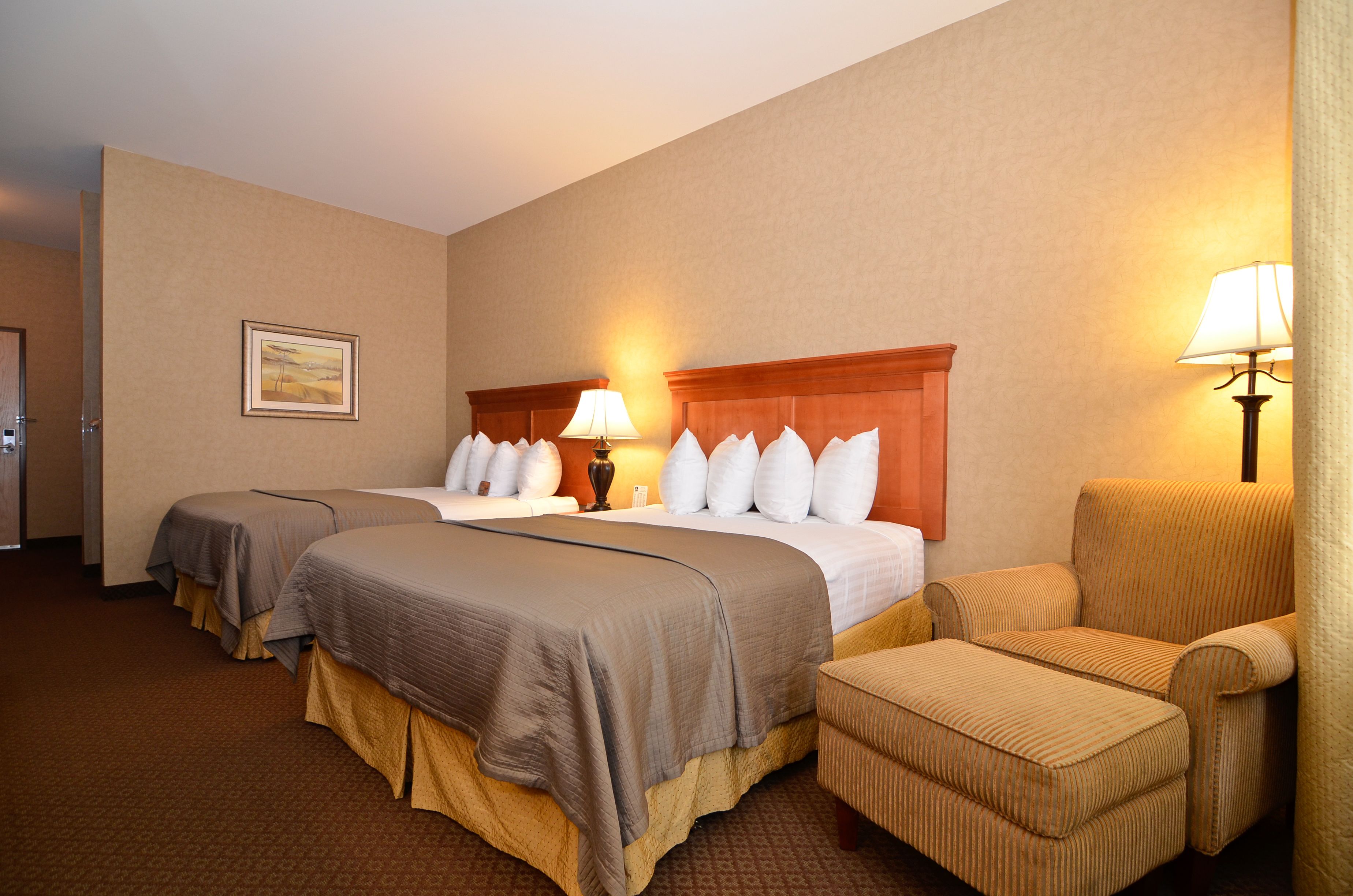 A hotel room with two beds, a chair, and a lamp.