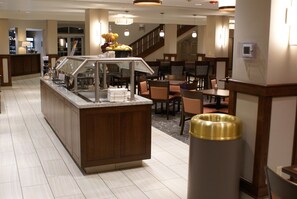 A hotel lobby with a self-service food station, seating area, and a staircase.