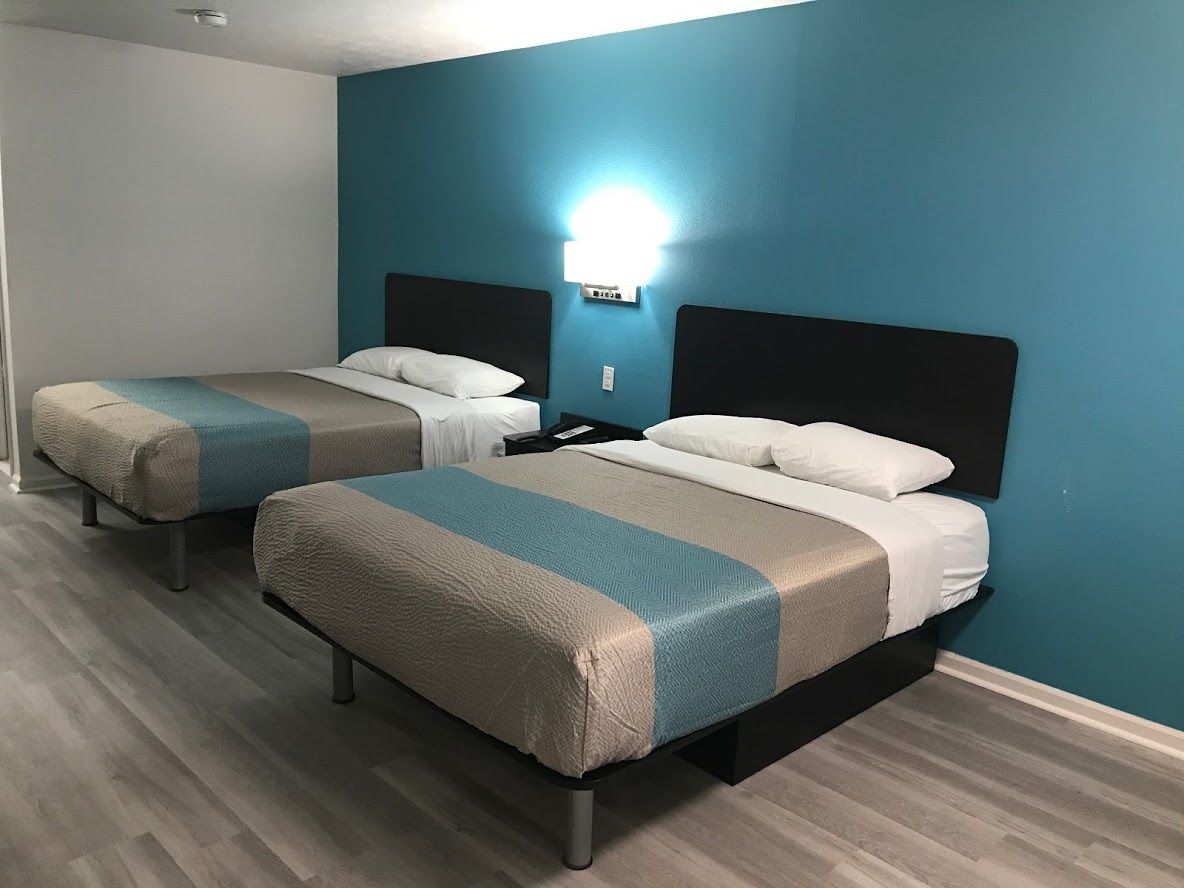Una habitación de hotel con dos camas, una mesita de noche y una lámpara de pared.