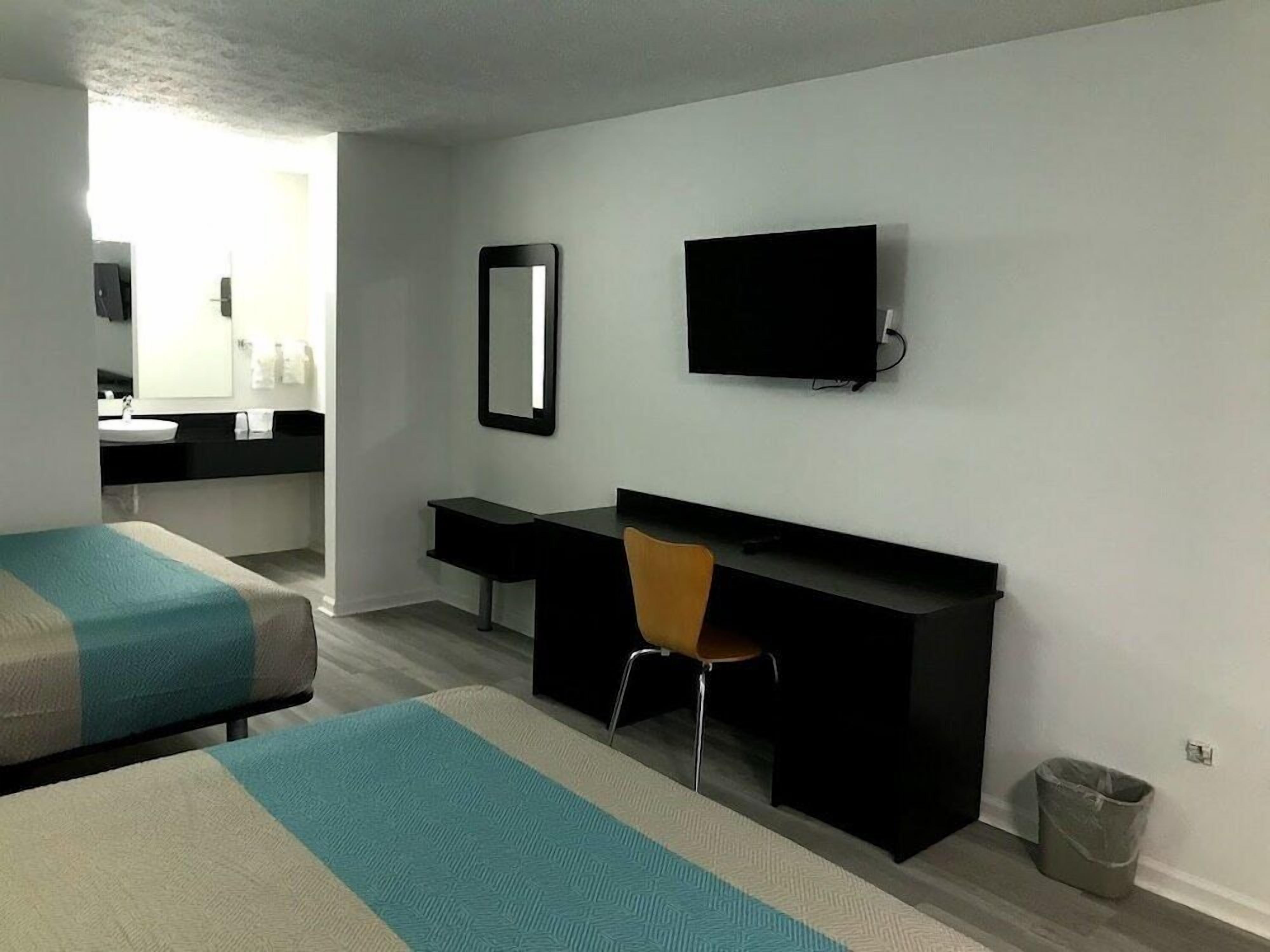 Une chambre d’hôtel avec deux lits, un bureau, une chaise, une télévision et une salle de bain visible à travers une porte ouverte.