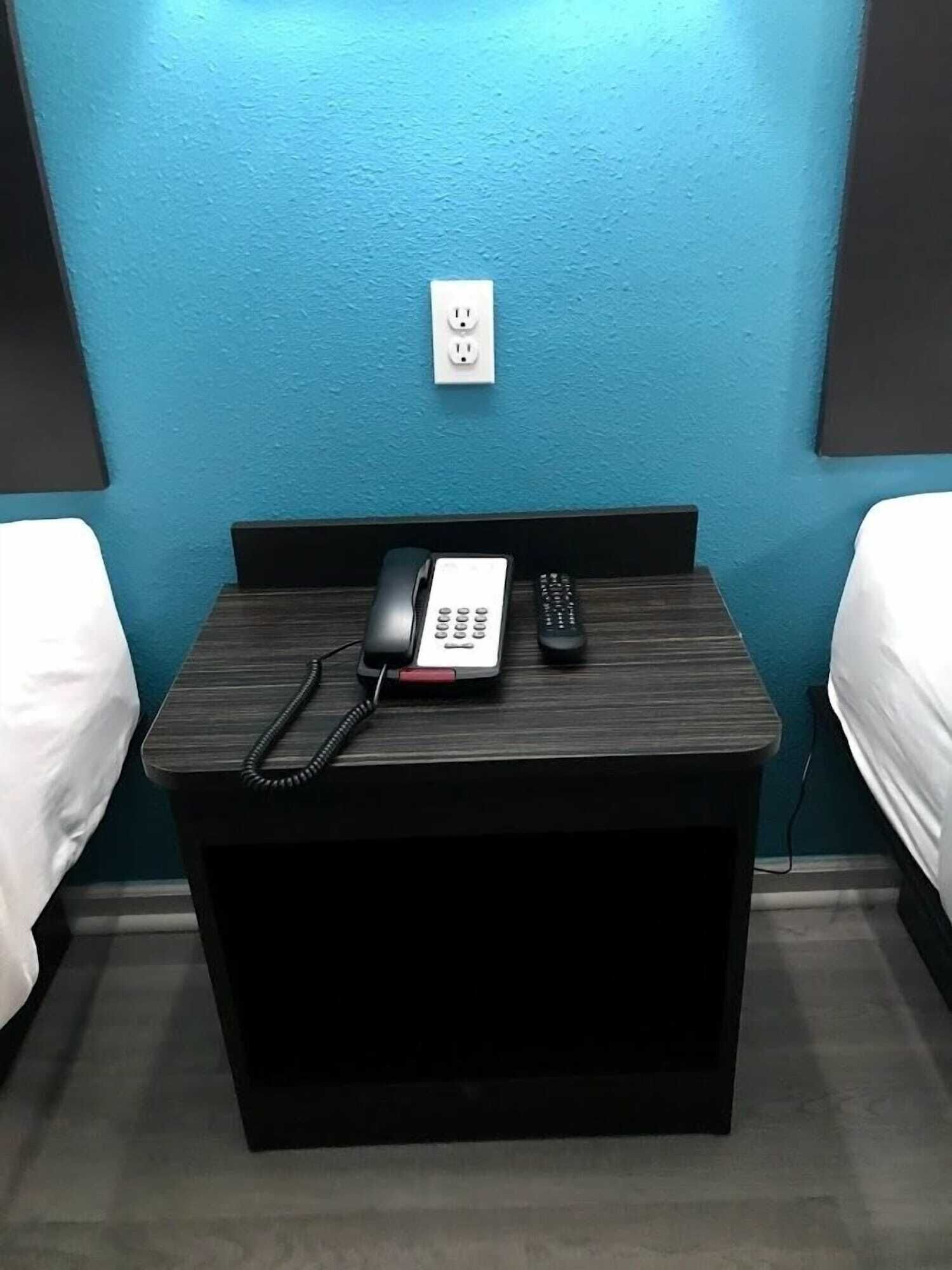 A hotel room with a wooden nightstand, a telephone, and a remote control.
