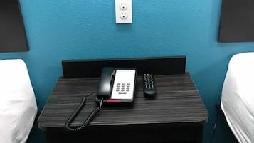 A hotel room with a wooden nightstand, a telephone, and a remote control.