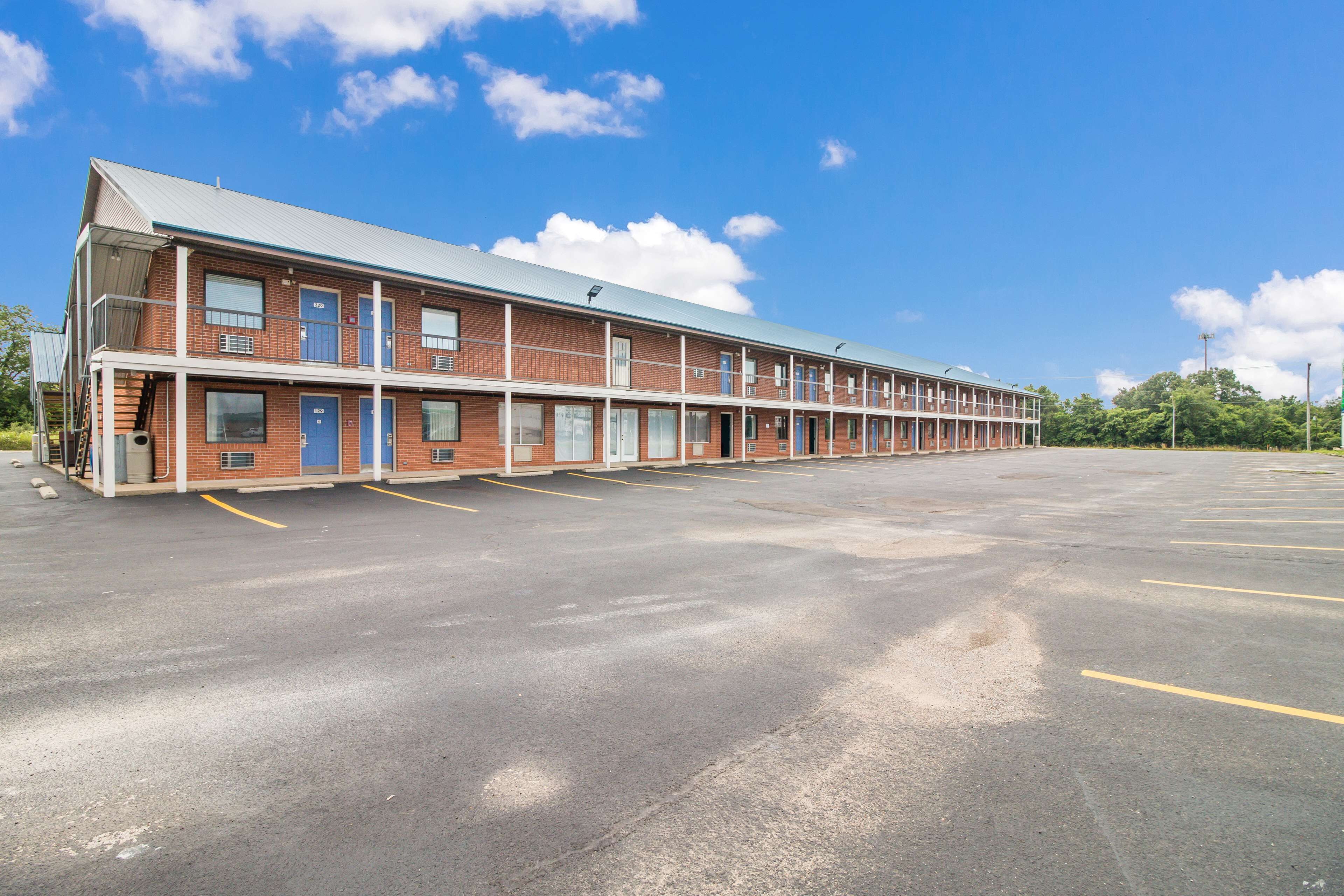A long, single-story motel with a row of rooms on one side and a large parking lot in front.