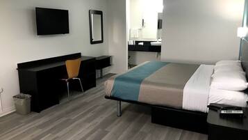 A modern hotel room with a bed, a desk, a chair, a TV, and a bathroom visible through an open door.