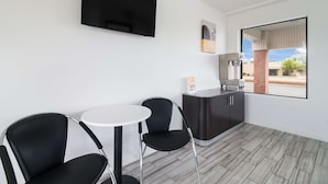 A small room with a flat-screen TV mounted on the wall, a small table with two chairs, a dark-colored cabinet, and a window with a view of the outside. - Motel 6 Metropolis, IL (Metropolis)