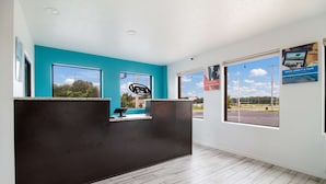 A reception area with a black counter, teal walls, and large windows offering views of a parking lot and greenery. - Motel 6 Metropolis, IL (Metropolis)