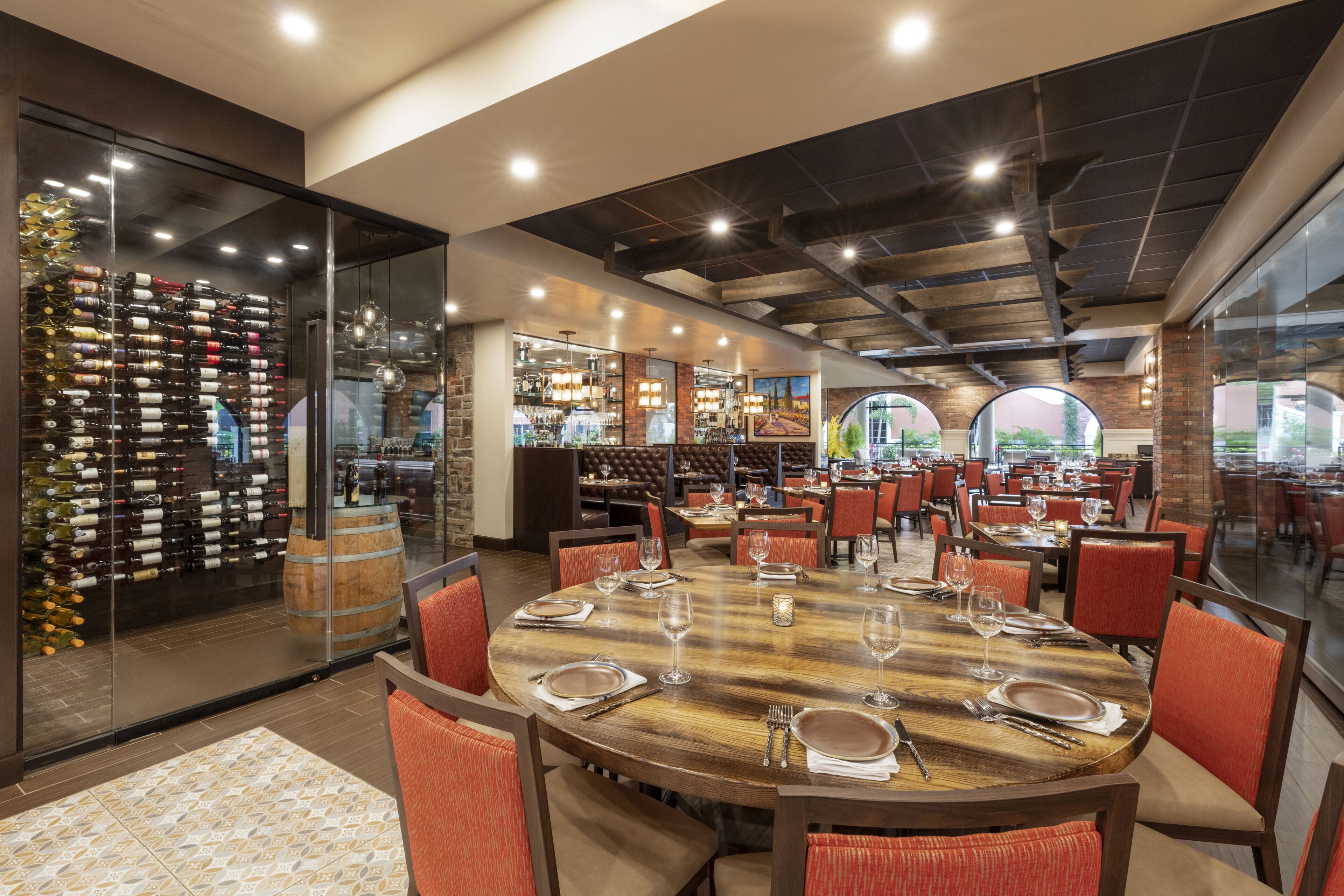 Un restaurant avec une grande table en bois dressée pour le repas, entourée de chaises à revêtement rouge.