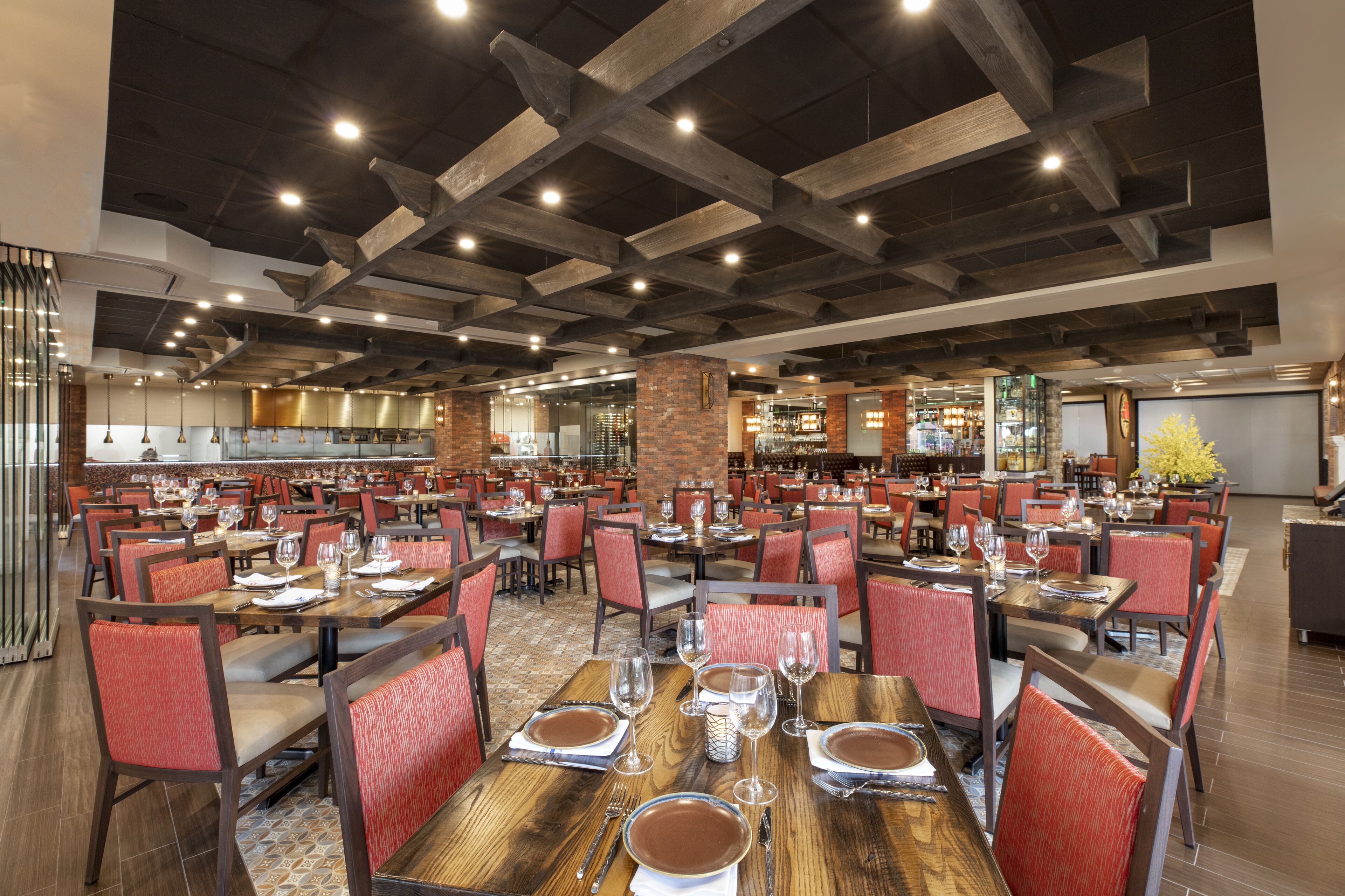 A spacious restaurant with multiple dining tables and chairs, a brick accent wall, and a modern ceiling design.