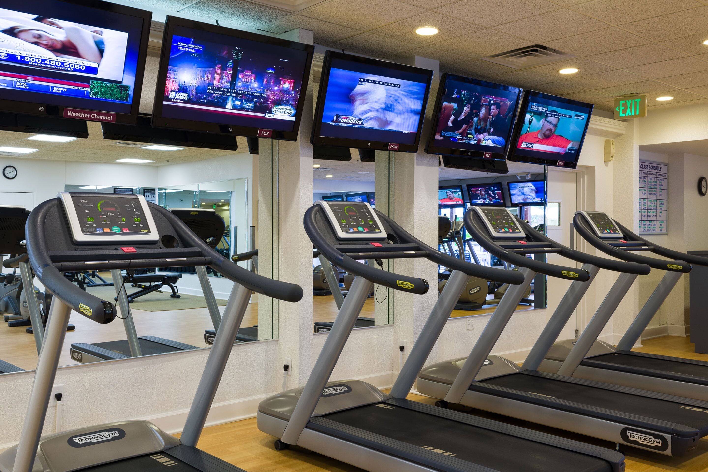 Une salle de sport équipée de tapis de course, d’appareils d’exercice et de plusieurs écrans de télévision diffusant des chaînes d’information.