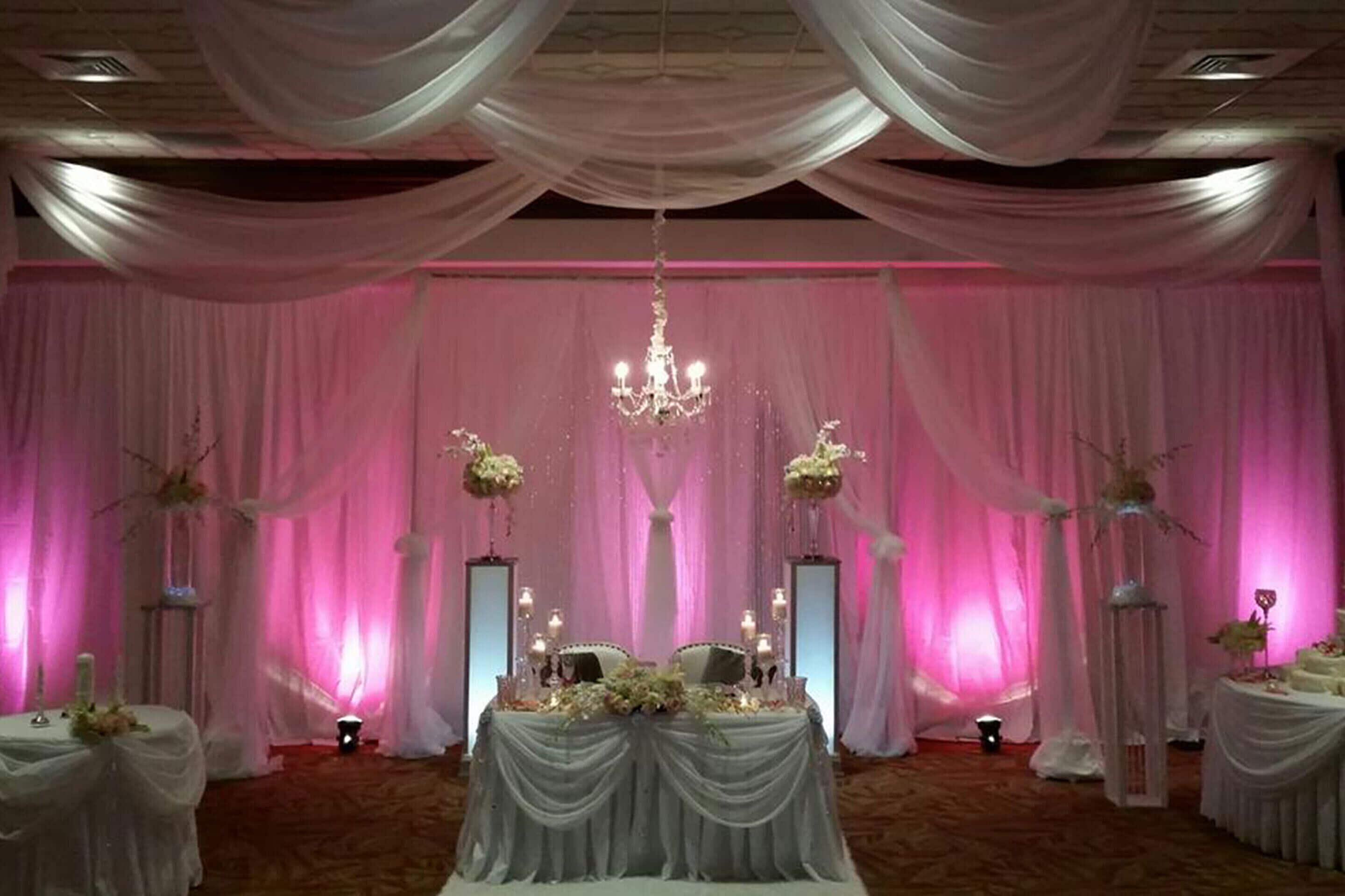 Salón para recepción de bodas con escenario, cortinas decorativas y arreglos florales.
