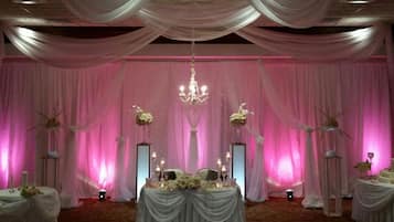 Salón para recepción de bodas con escenario, cortinas decorativas y arreglos florales.