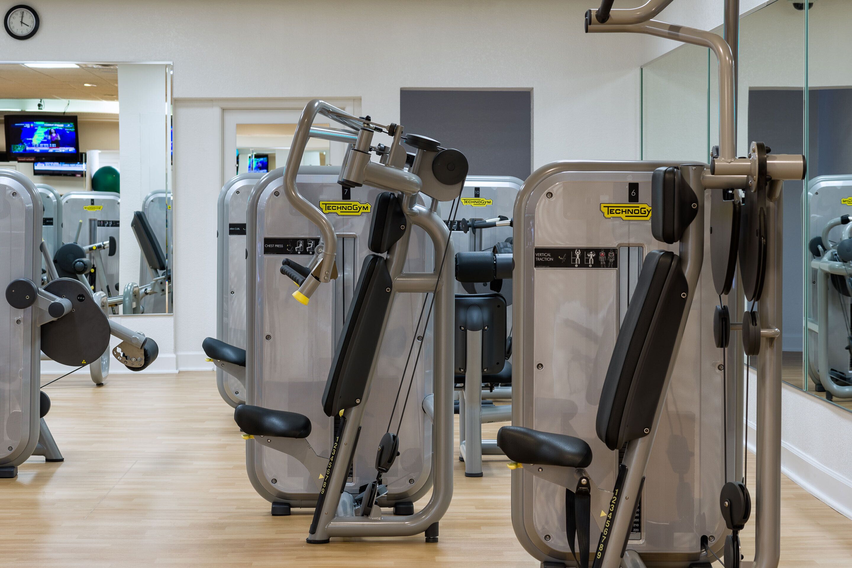 A gym with cardio machines, weight machines, and a television displaying a sports event.
