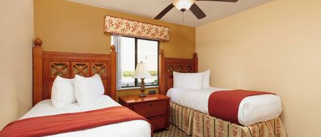 A hotel room with two beds, a ceiling fan, a window with a view, and a nightstand with a lamp.