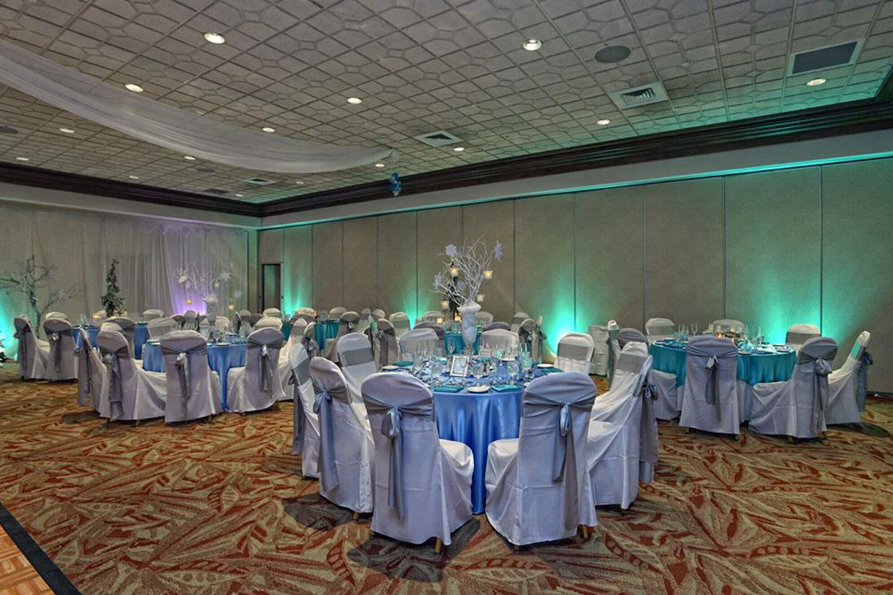 Un salón de banquetes con mesas redondas, sillas blancas y manteles azules.
