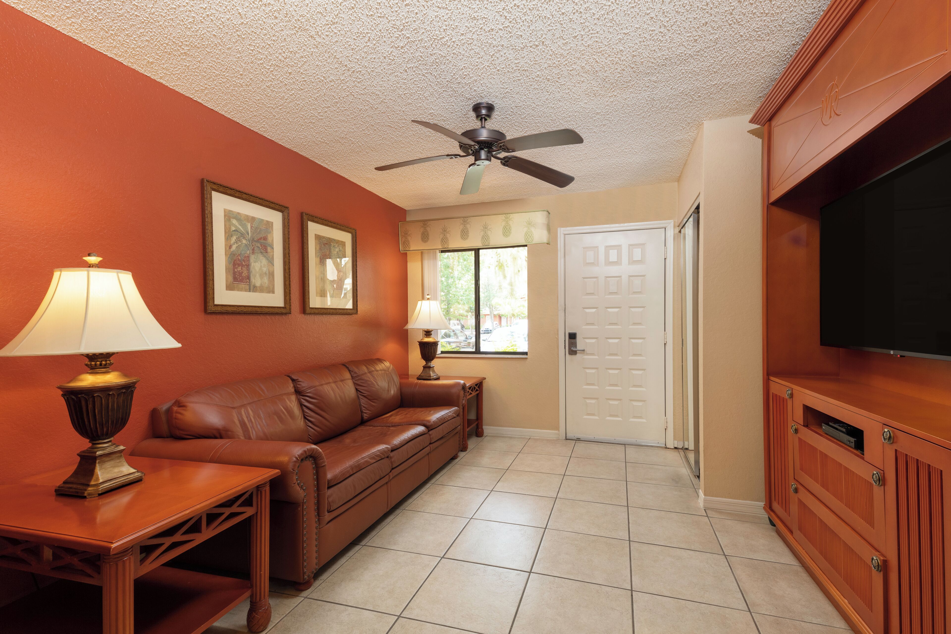 A living room with a brown leather sofa, a wooden coffee table, a ceiling fan, and a television on a wooden cabinet.