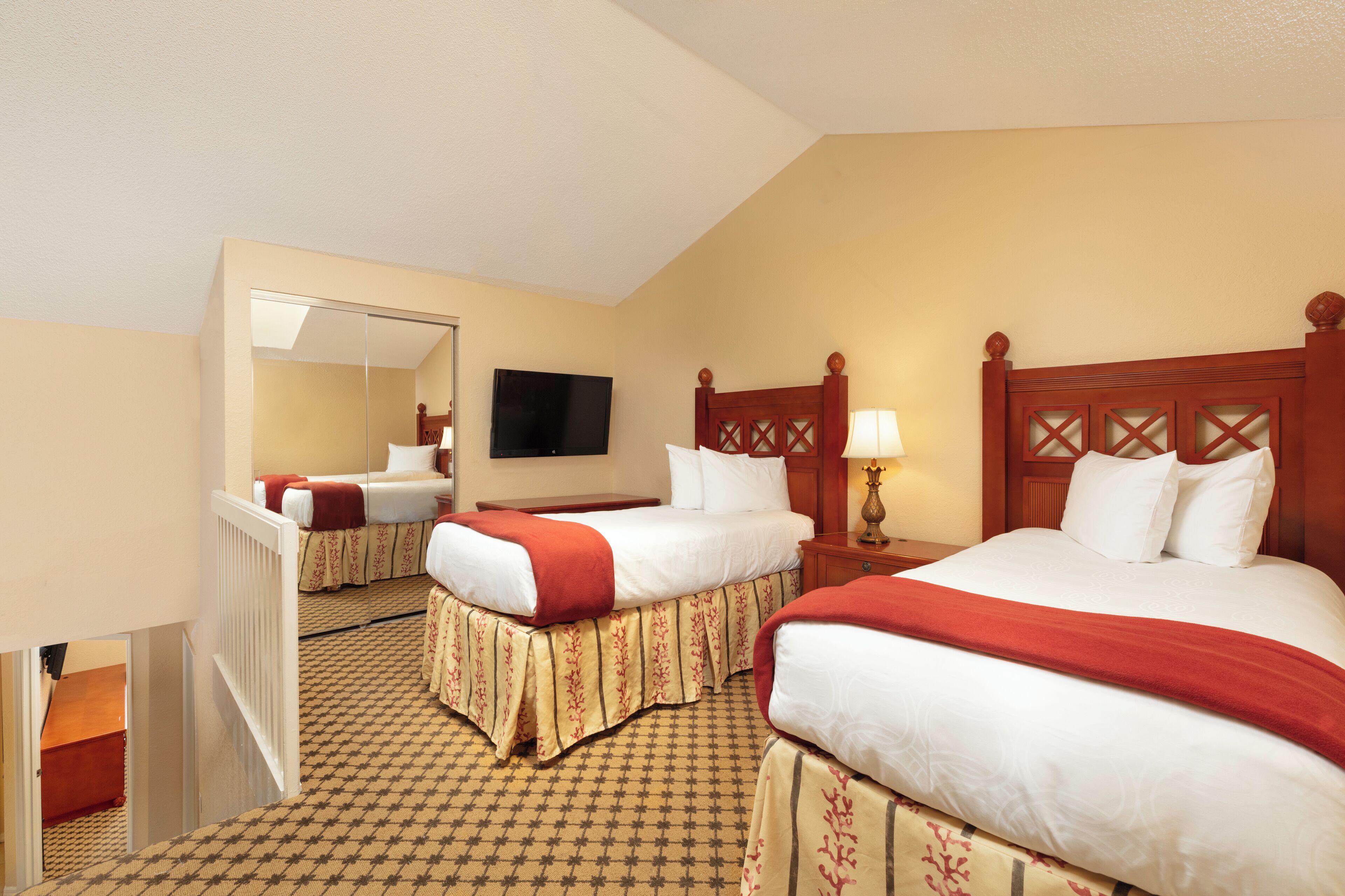 A hotel room with two beds, a television, and a mirror.