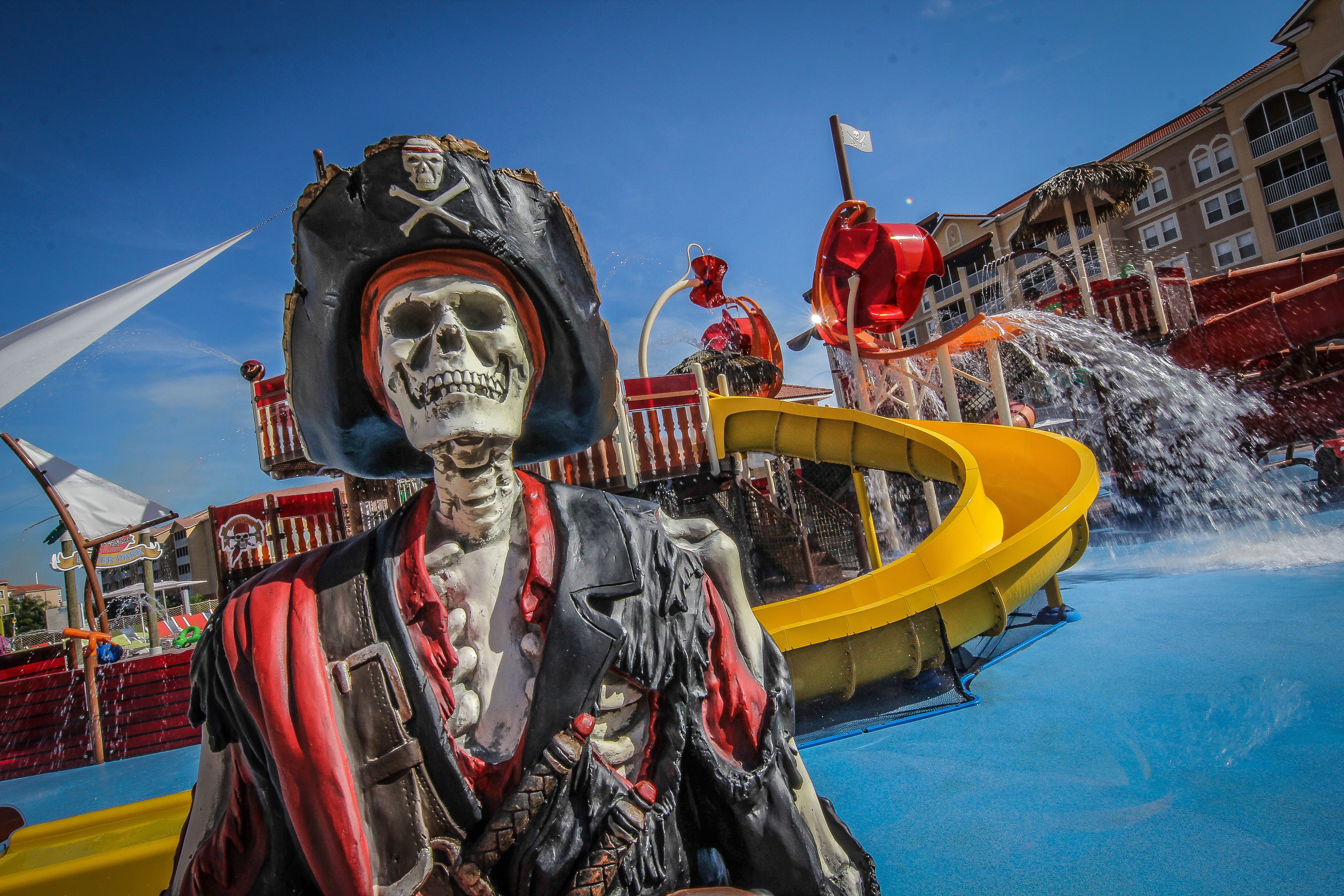 A pirate-themed water park with a large skeleton figure, water slides, and a pool.