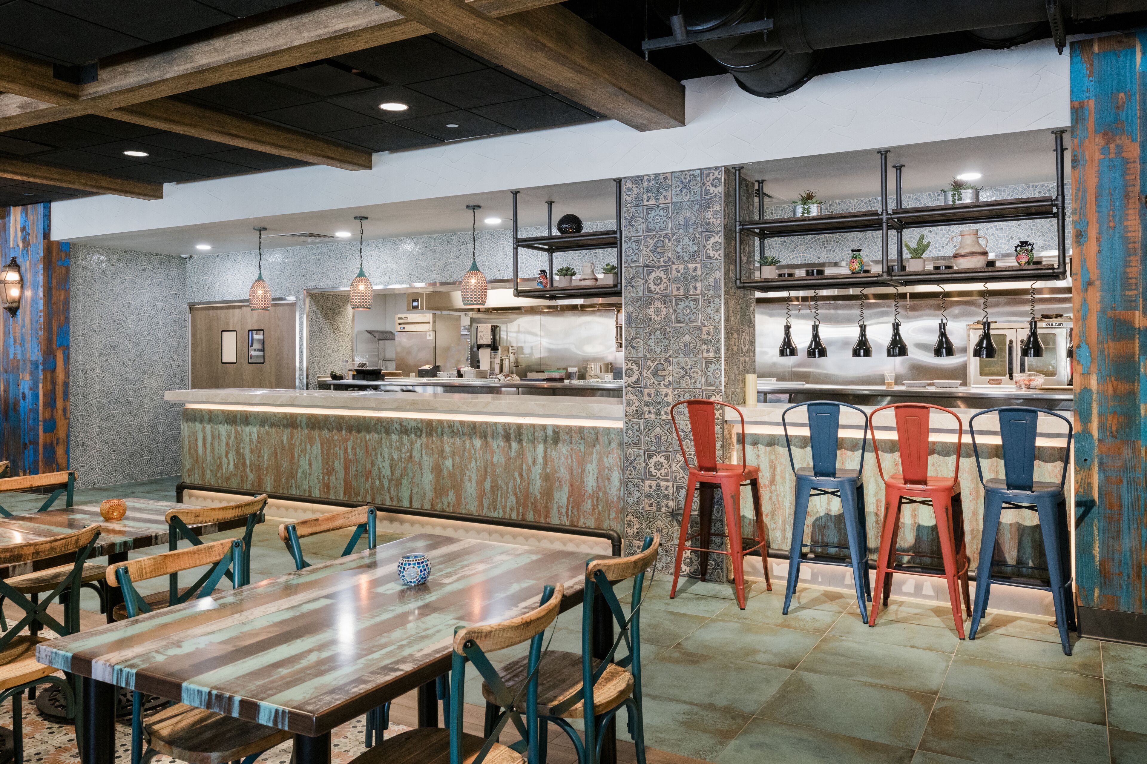 Un ristorante con tavoli e sedie in legno, un'area bar e una cucina sullo sfondo.