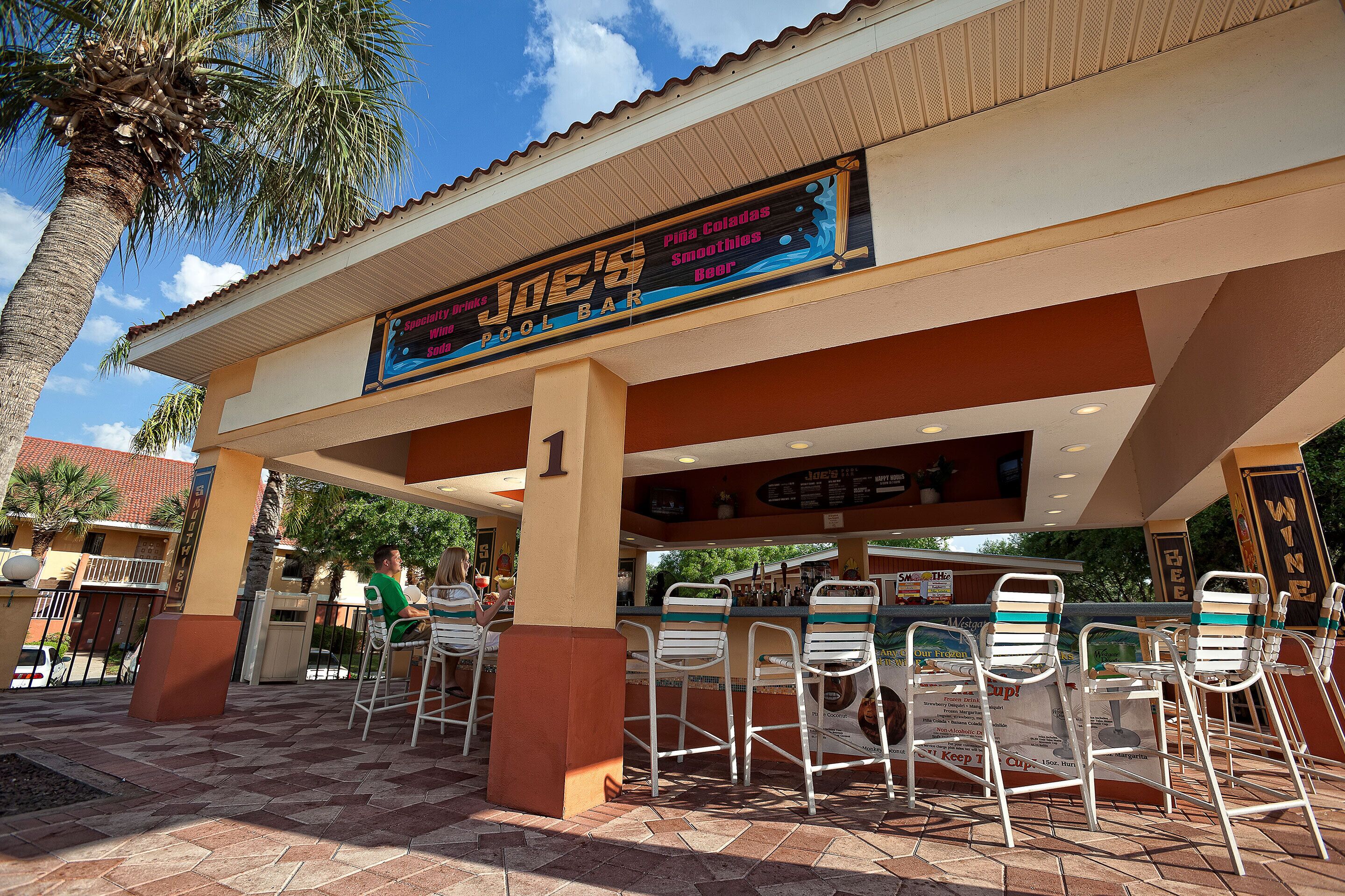 An outdoor bar with a signboard, seating area, and palm trees.