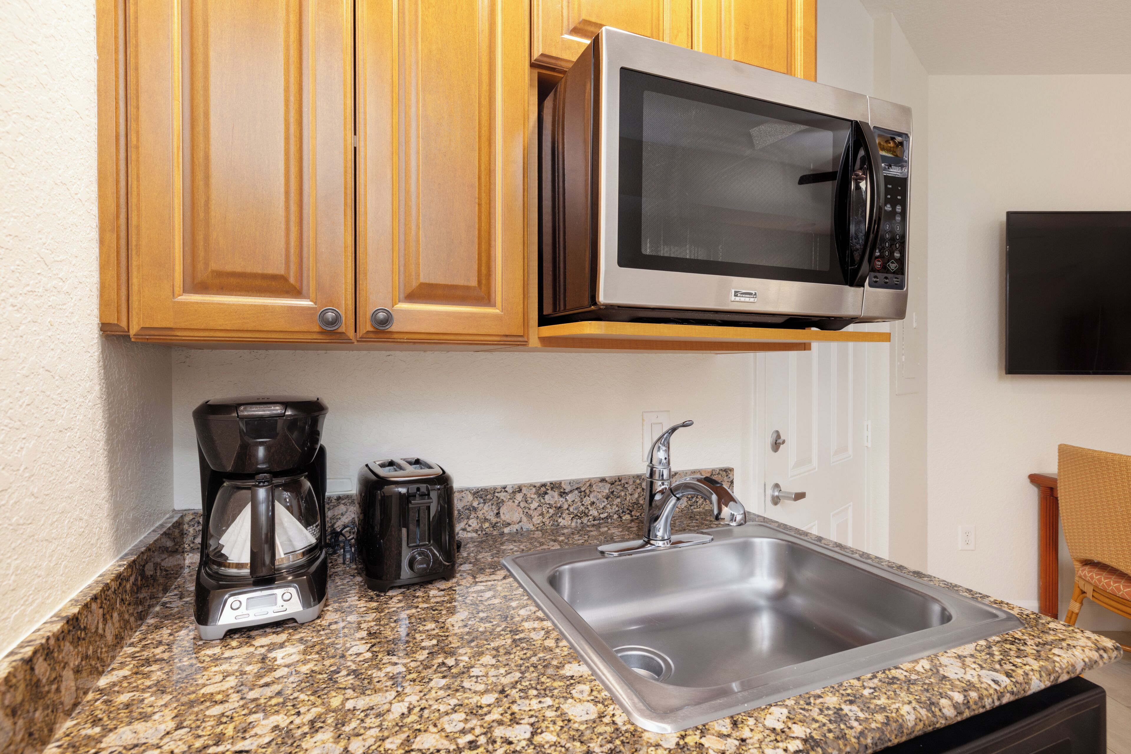 A kitchen with wooden cabinets, a stainless steel sink, a microwave, a coffee maker, and a toaster.