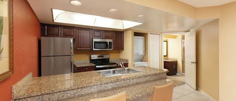 A kitchen with granite countertops, stainless steel appliances, and wicker chairs.