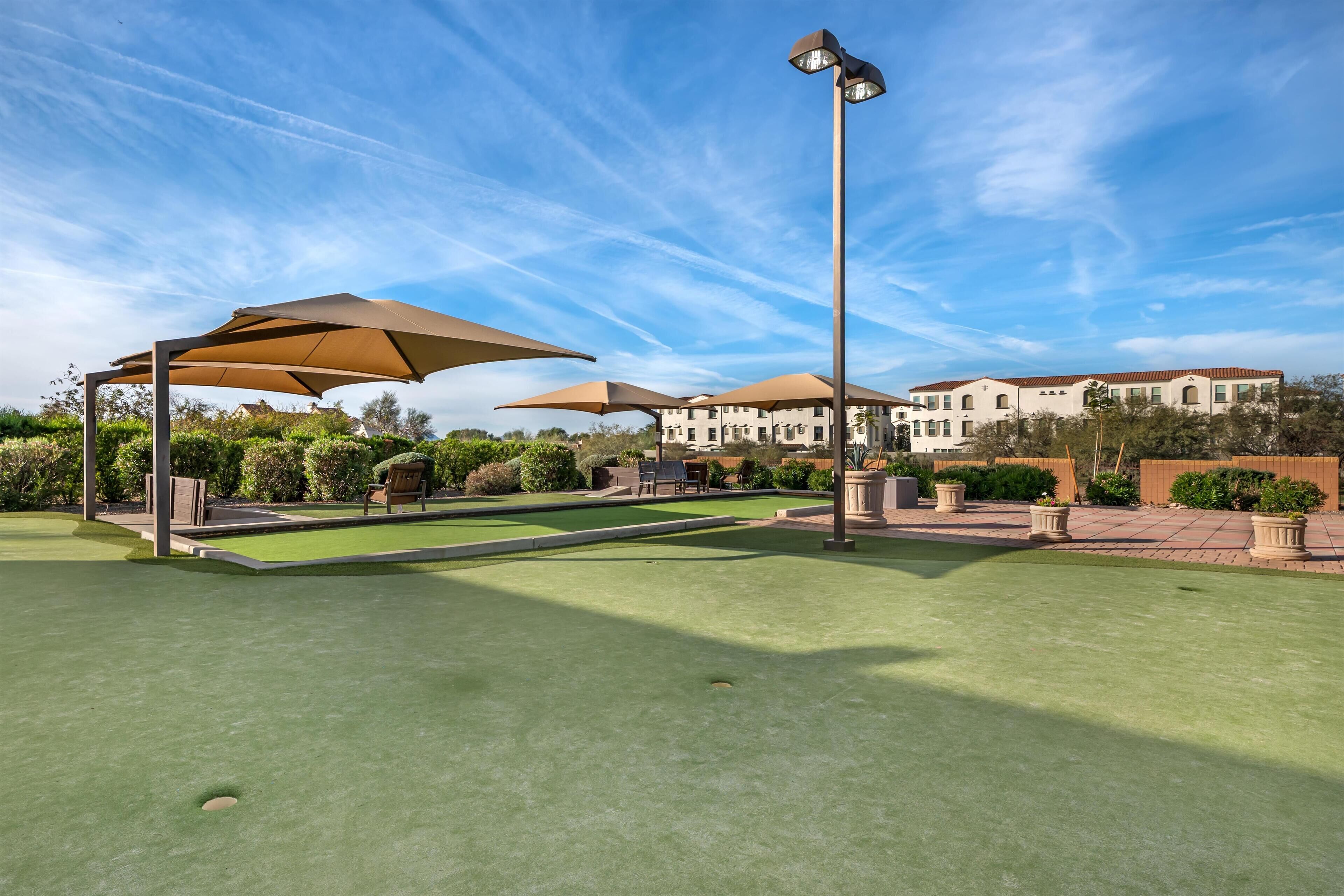 A golf course with multiple umbrellas, a lamp post, and a building in the background.