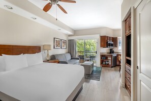 A hotel room with a large bed, a ceiling fan, a sofa, a desk with a lamp, and a view of the outside.