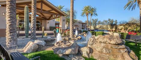 Un resort con palmeras, un jardín de rocas y un patio techado.
