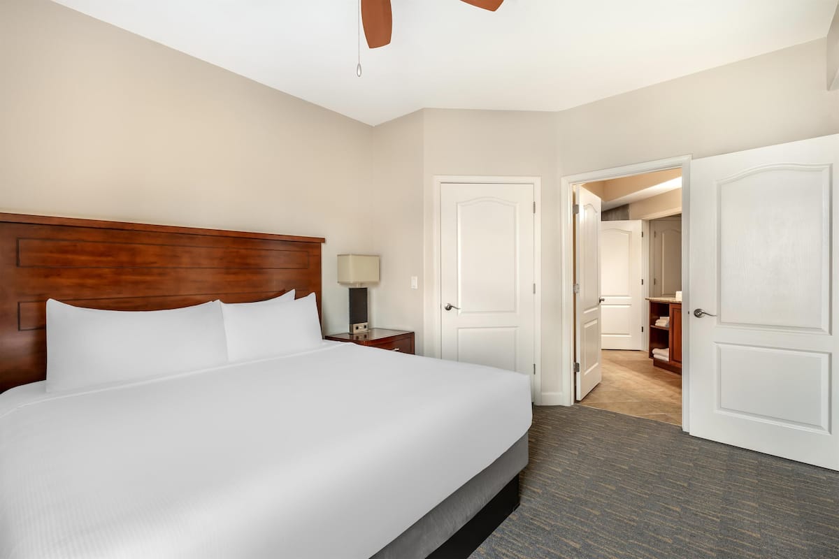 Hotelkamer met een groot bed, houten hoofdeinde, witte muren en een vloerbedekking.