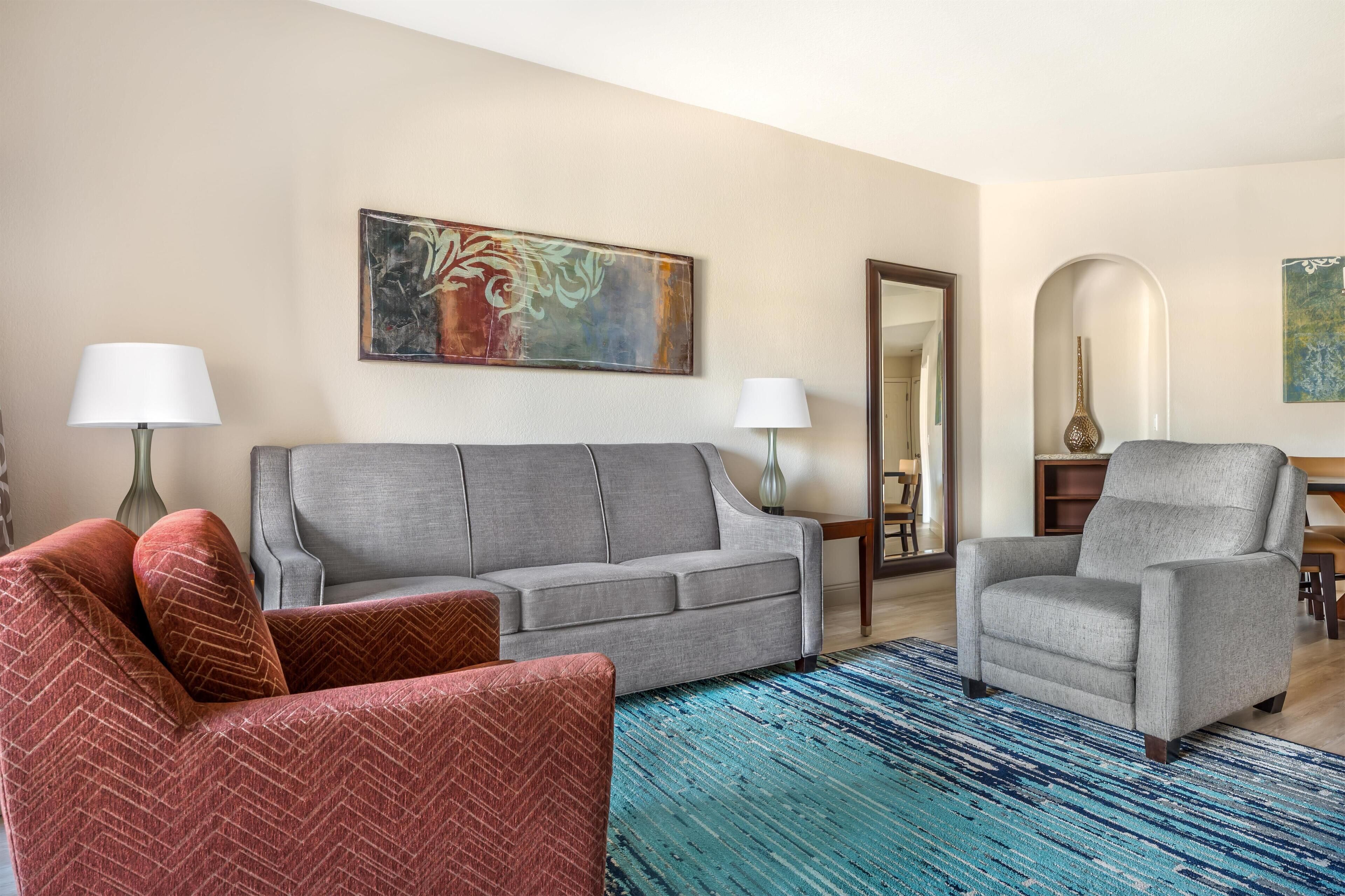 Una sala de estar con un sofá gris, un sillón rojo y un tapete azul estampado.