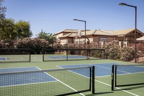 A tennis court with a net, surrounded by a fence and trees.
