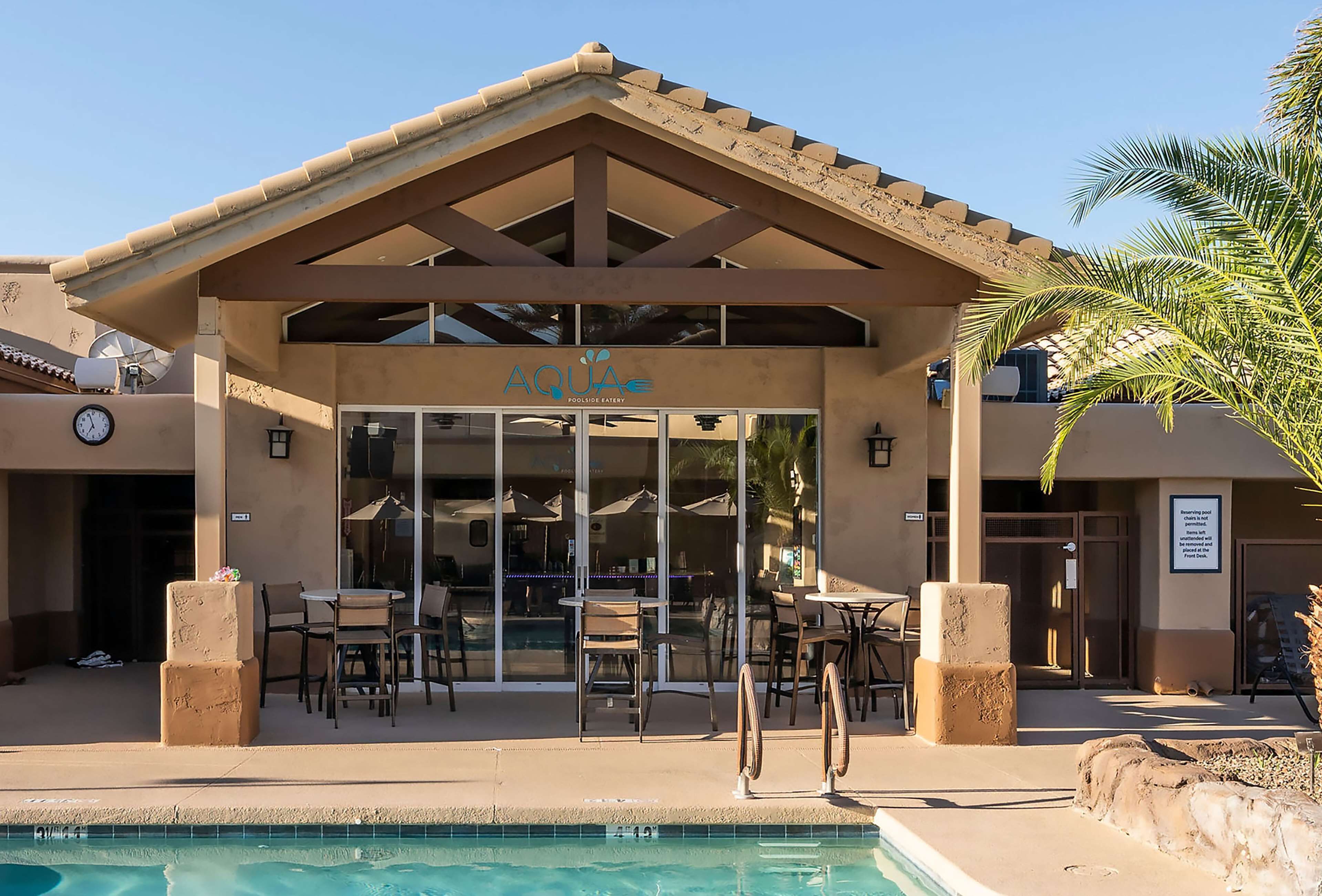 A poolside area with a covered seating area, a pool, and a sign reading "AQUA POOLSIDE BATHYRY".