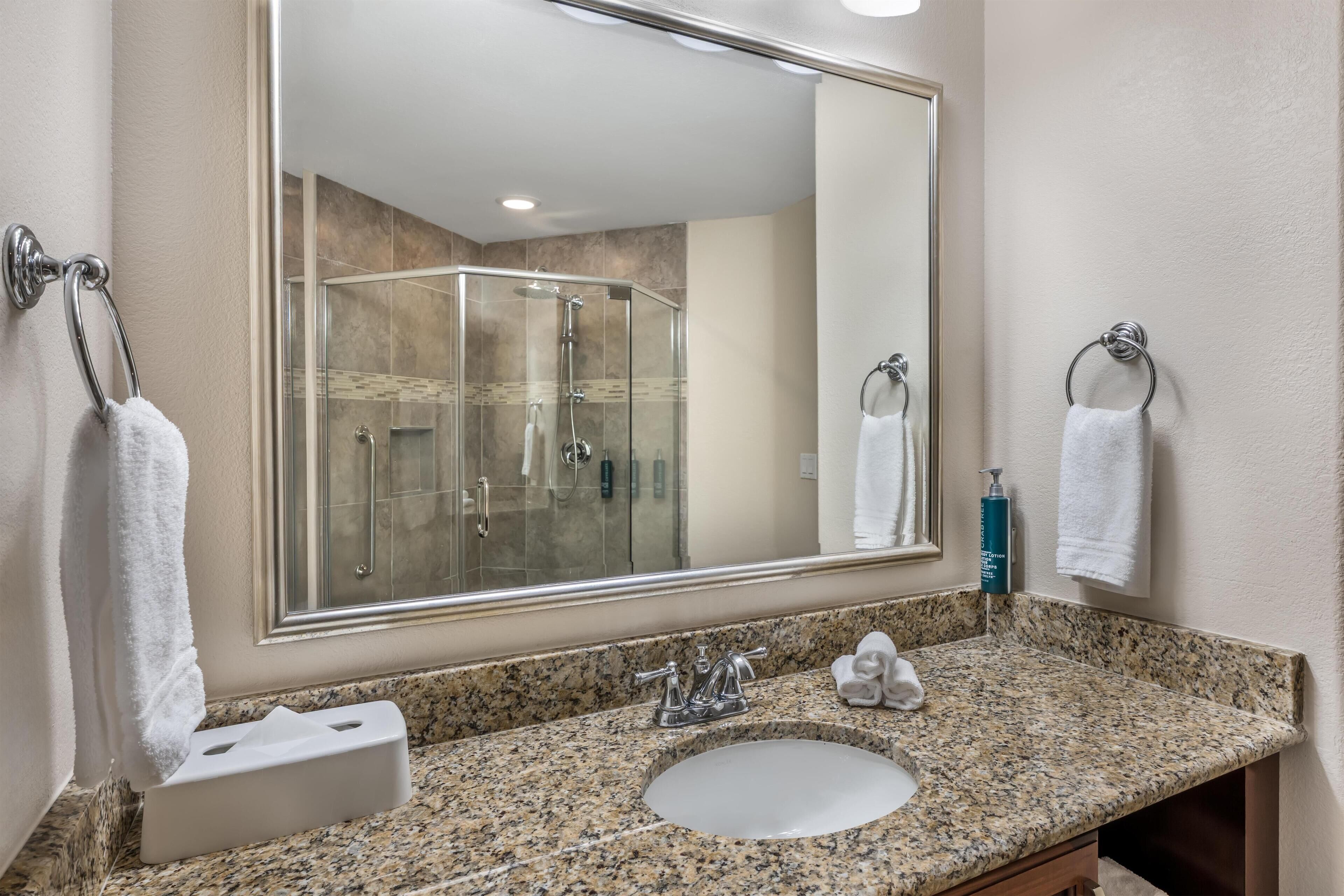 A bathroom with a granite countertop, a sink, a mirror, and a glass shower enclosure.