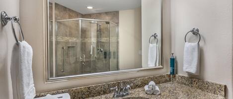 A bathroom with a granite countertop, a sink, a mirror, and a glass shower enclosure.