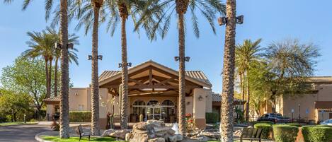A building with a covered entrance, palm trees, and a paved driveway.