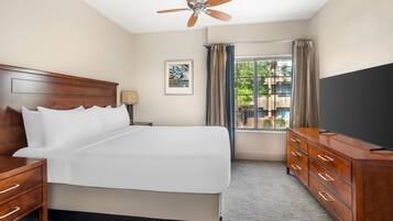 A hotel room with a large bed, wooden headboard, a dresser, a ceiling fan, a window with curtains, and a TV.