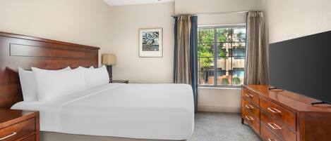A hotel room with a large bed, wooden headboard, a dresser, a ceiling fan, a window with curtains, and a TV.