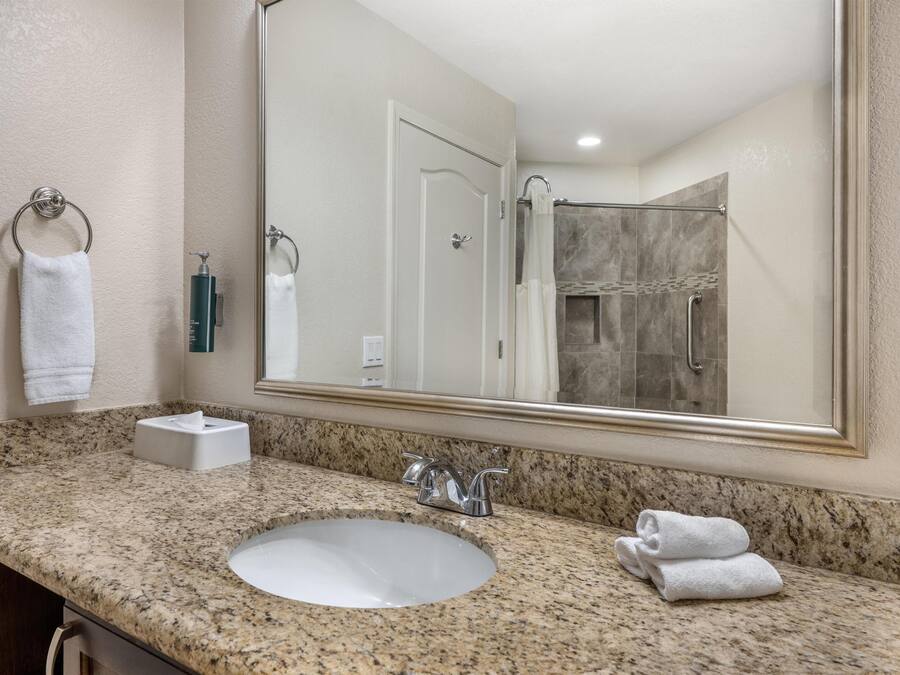 A bathroom with a granite countertop, a white sink, a large mirror, and a shower area.