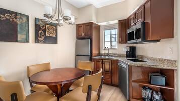 A compact kitchen with wooden cabinets, a stainless steel refrigerator, a microwave, and a built-in oven. There is a dining table with chairs and a chandelier.